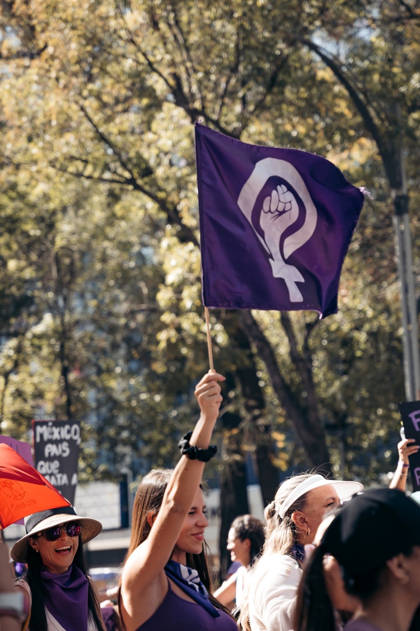 En kvinne holder et banner høyt opp. Rundt henne er det flere kvinner som går i tog.